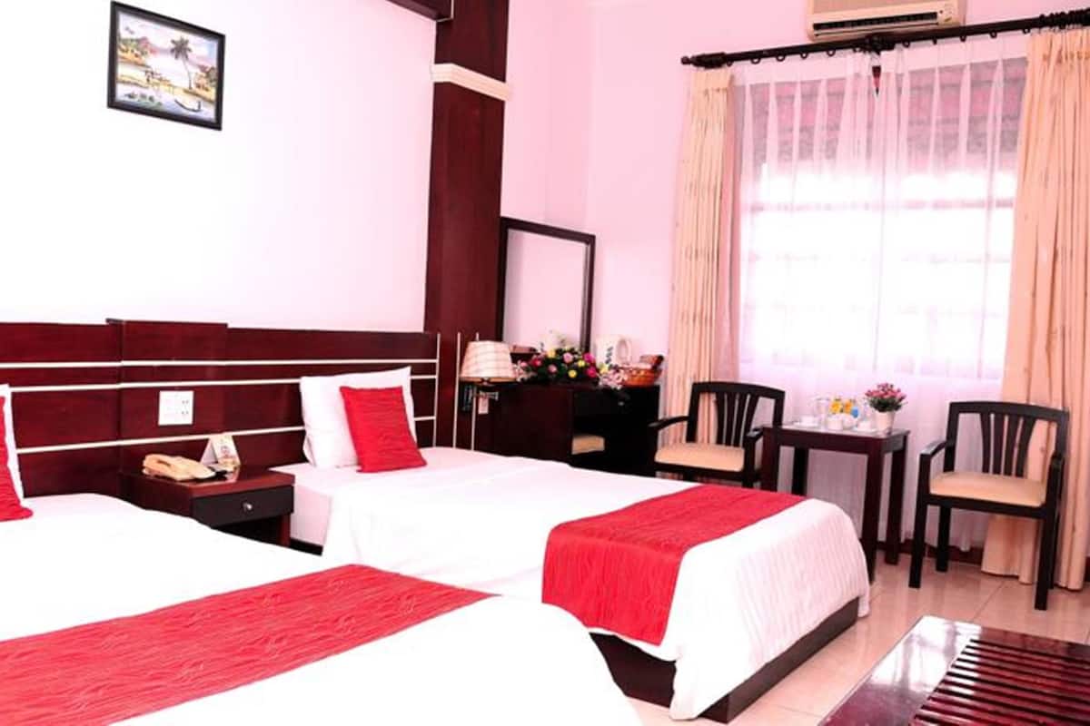 Habitación de hotel con dos camas, un escritorio, sillas y una ventana con cortinas.