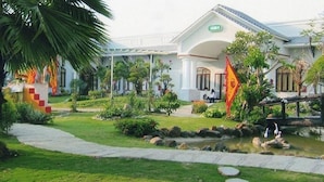 A hotel with a garden pathway leading to a pond, surrounded by greenery and palm trees. - Cuu Long Hotel (Can Tho)