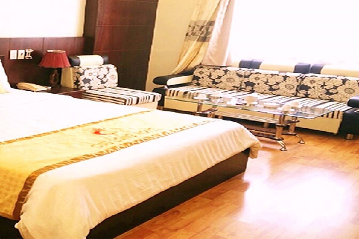 Habitación Deluxe Plus con una cama grande, un sofá, una mesita de noche y una lámpara.