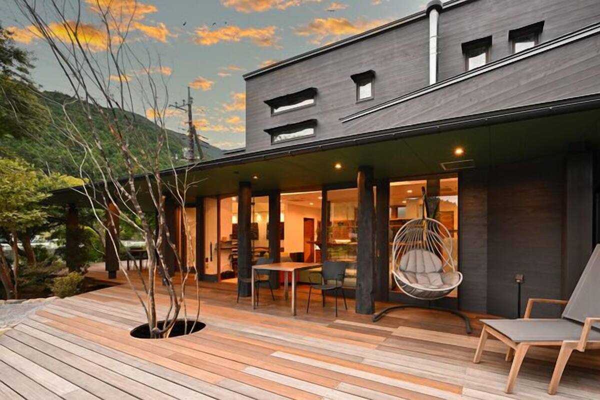 A modern building with a wooden deck, outdoor seating, and a hanging chair.