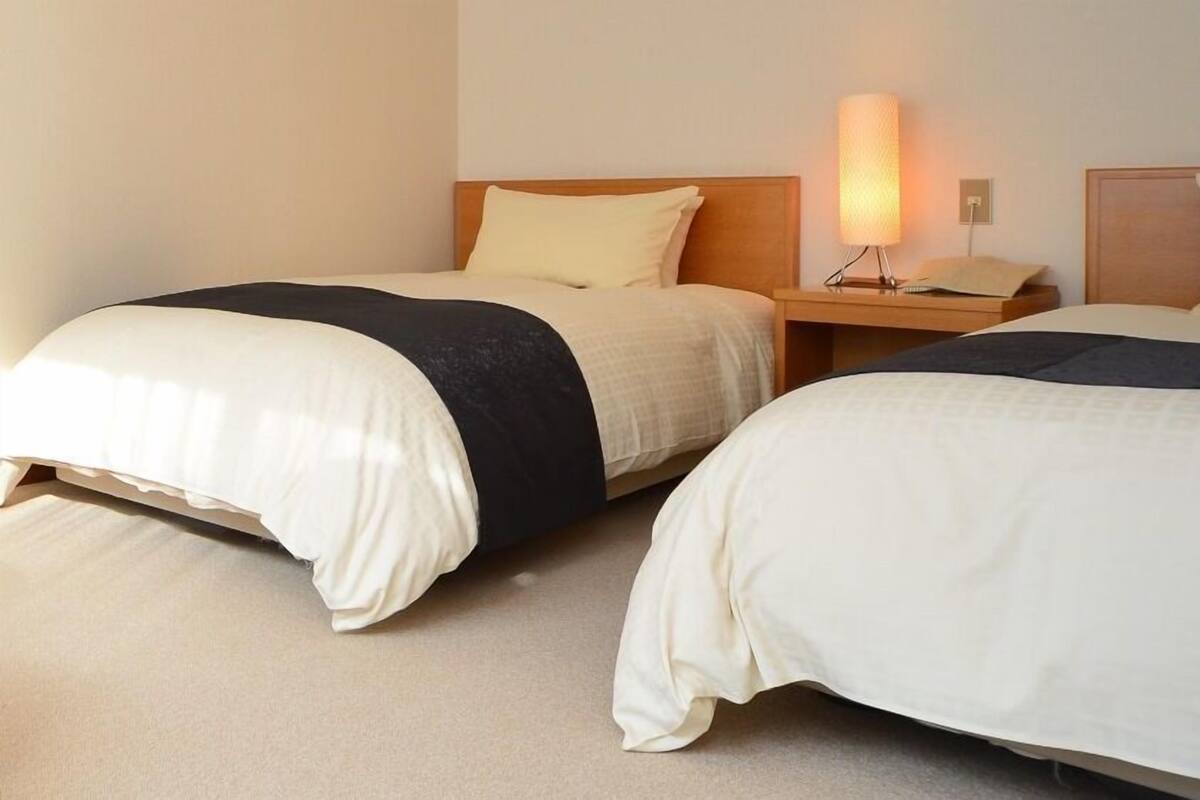 Two beds with headboards, a bedside table with a lamp, and a wall socket.