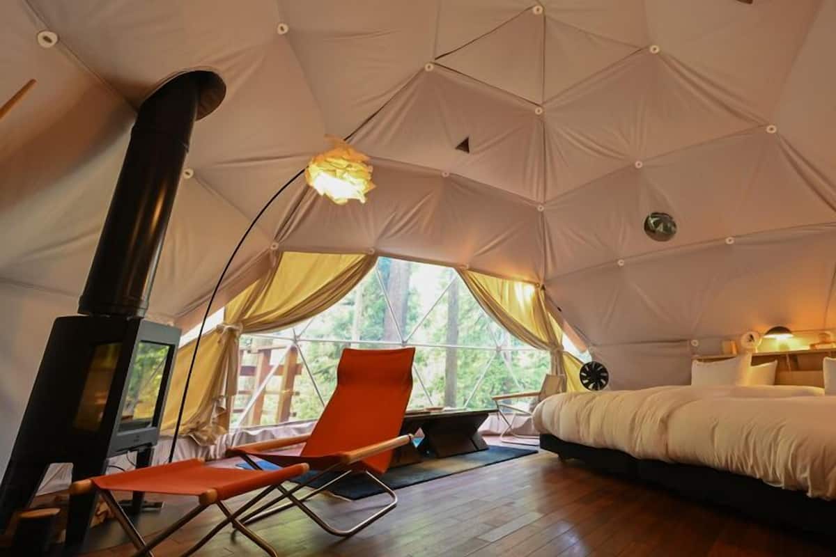 A tent with a bed, a chair, a table, and a fireplace.