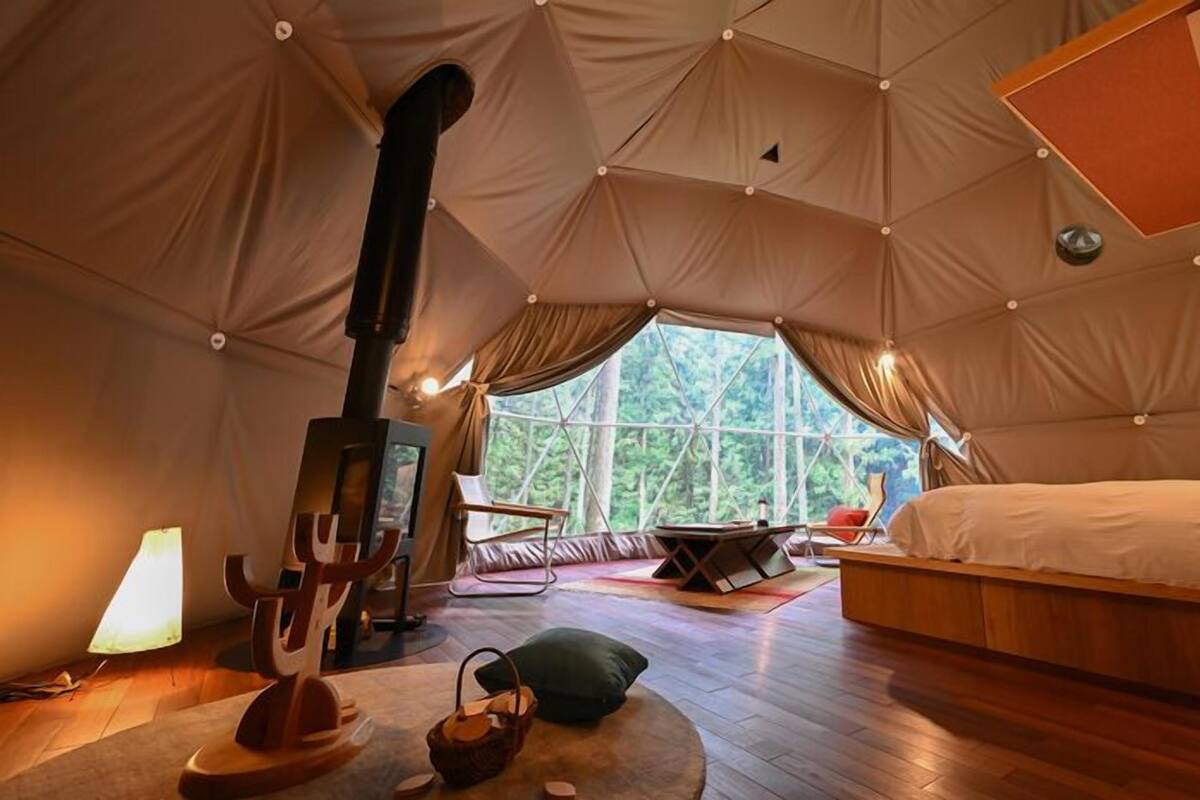 A tented room with a bed, a table, a chair, a lamp, and a fireplace.