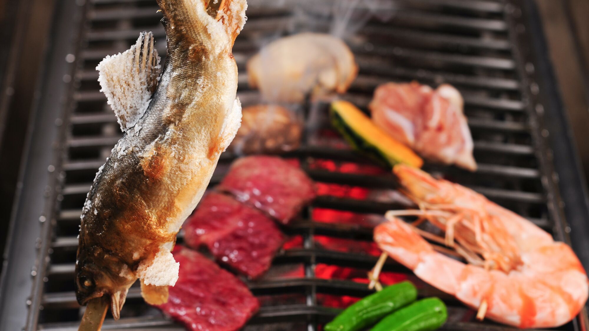 A fish being grilled on a grill with other meats and vegetables.