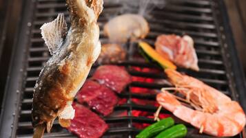 A fish being grilled on a grill with other meats and vegetables.
