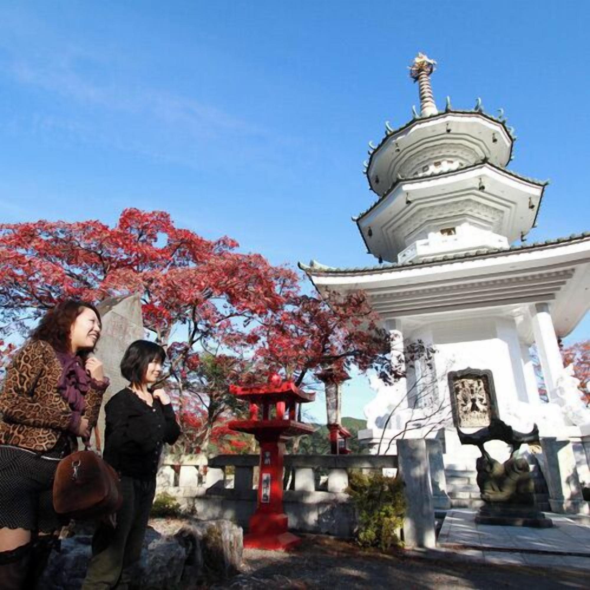 Una estructura de estilo pagoda con techo escalonado, rodeada de cerezos en flor y faroles de piedra.