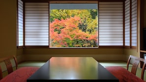 Una habitación con suelo de tatami, una mesa baja y un ventanal con vistas a follaje otoñal.