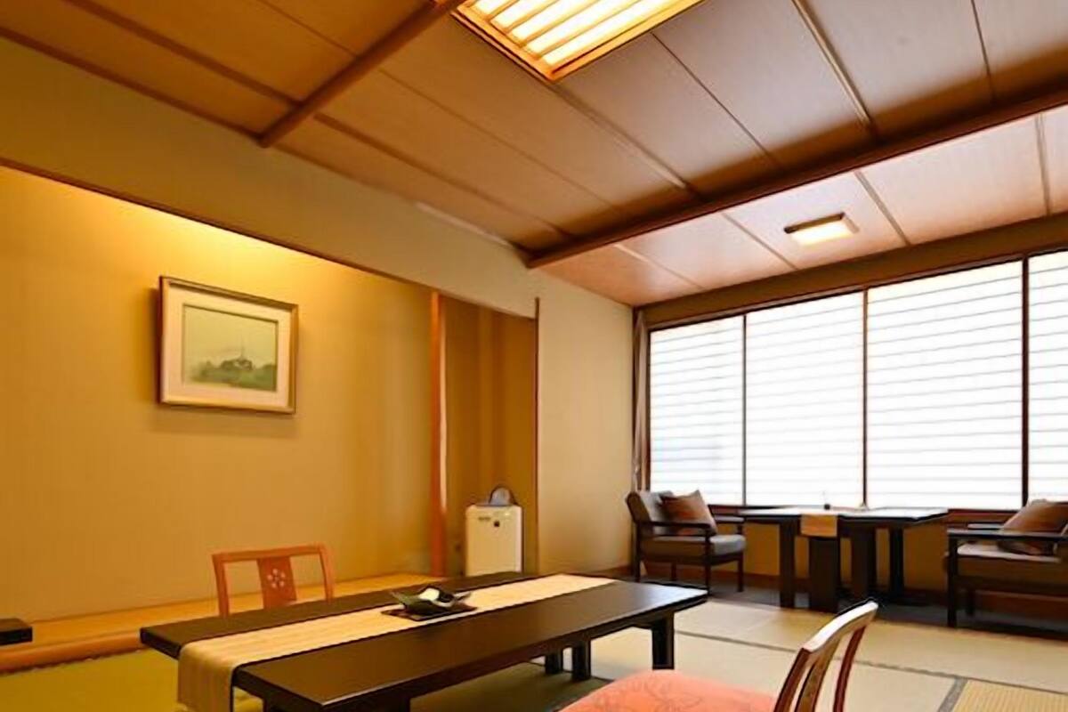 A tatami mat room with a low table, chairs, a small cabinet, and a window with blinds.