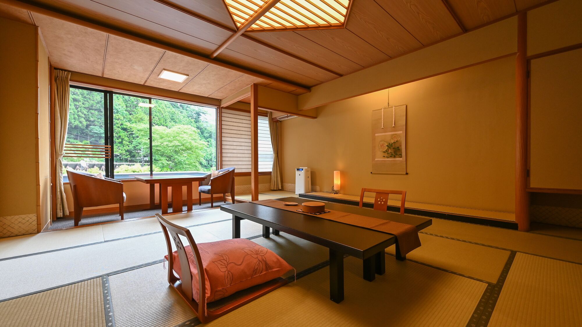 Une pièce de style japonais traditionnel, avec un sol recouvert de tatamis, une table basse, des chaises, une porte coulissante et une vue sur la verdure à l’extérieur.