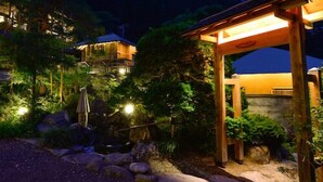 Une structure en bois, dotée d’un toit et entourée de rochers et de verdure, qui ressemble probablement à un jardin ou à un espace patio.