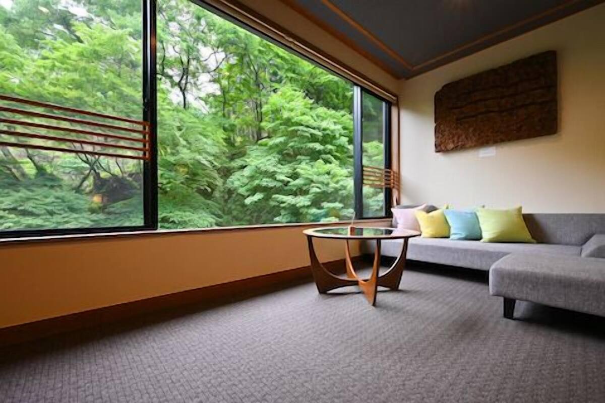 A room with a large window, a grey sofa, a small round table, and a wall-mounted artwork.
