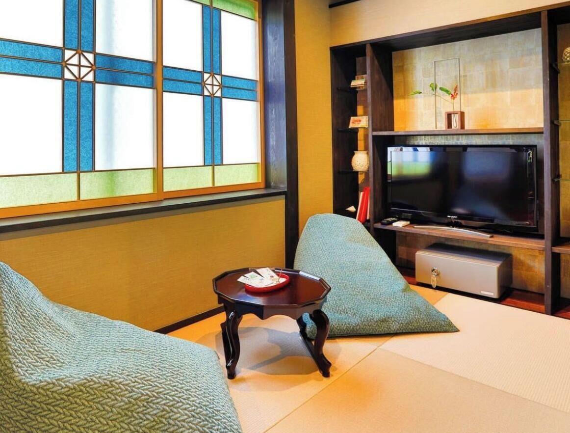 Una habitación tradicional japonesa con suelo de tatami, una mesa baja con una bandeja roja y un televisor.