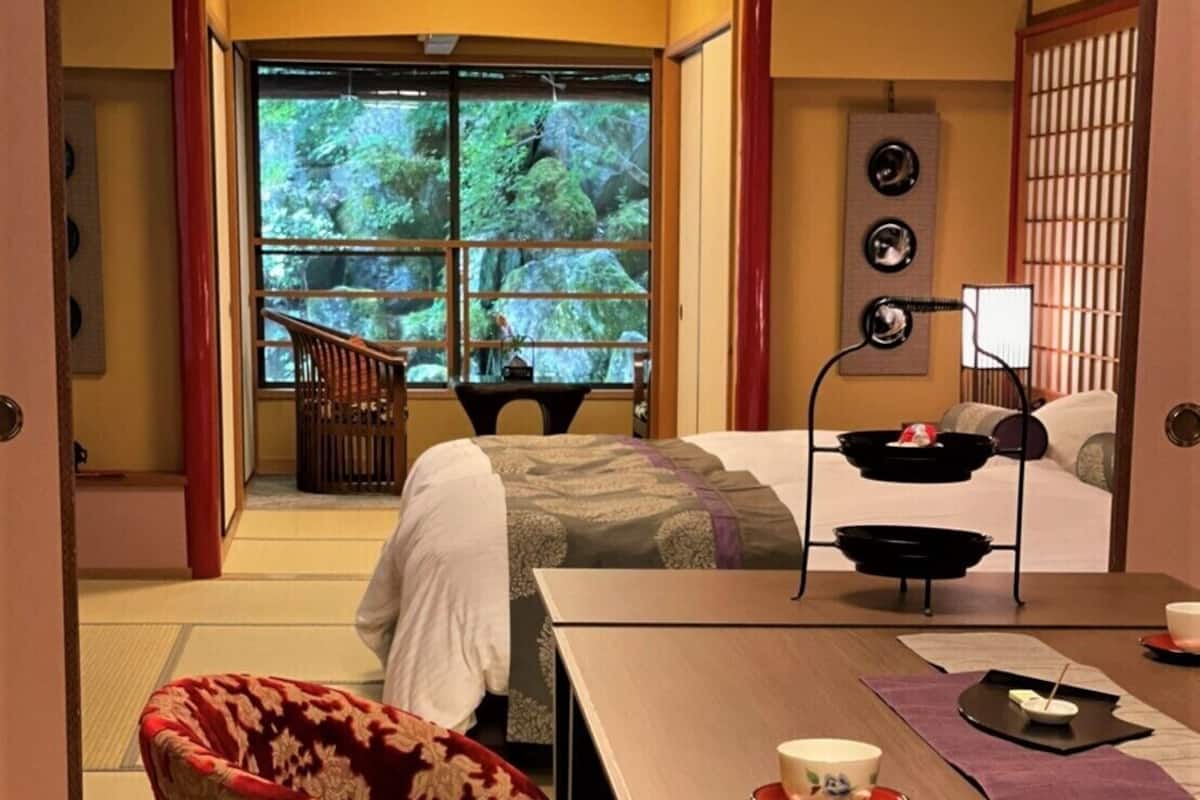 Una habitación tradicional japonesa con suelo de tatami, una mesa baja con un set de té y una puerta corrediza que da a un balcón con vistas a árboles.