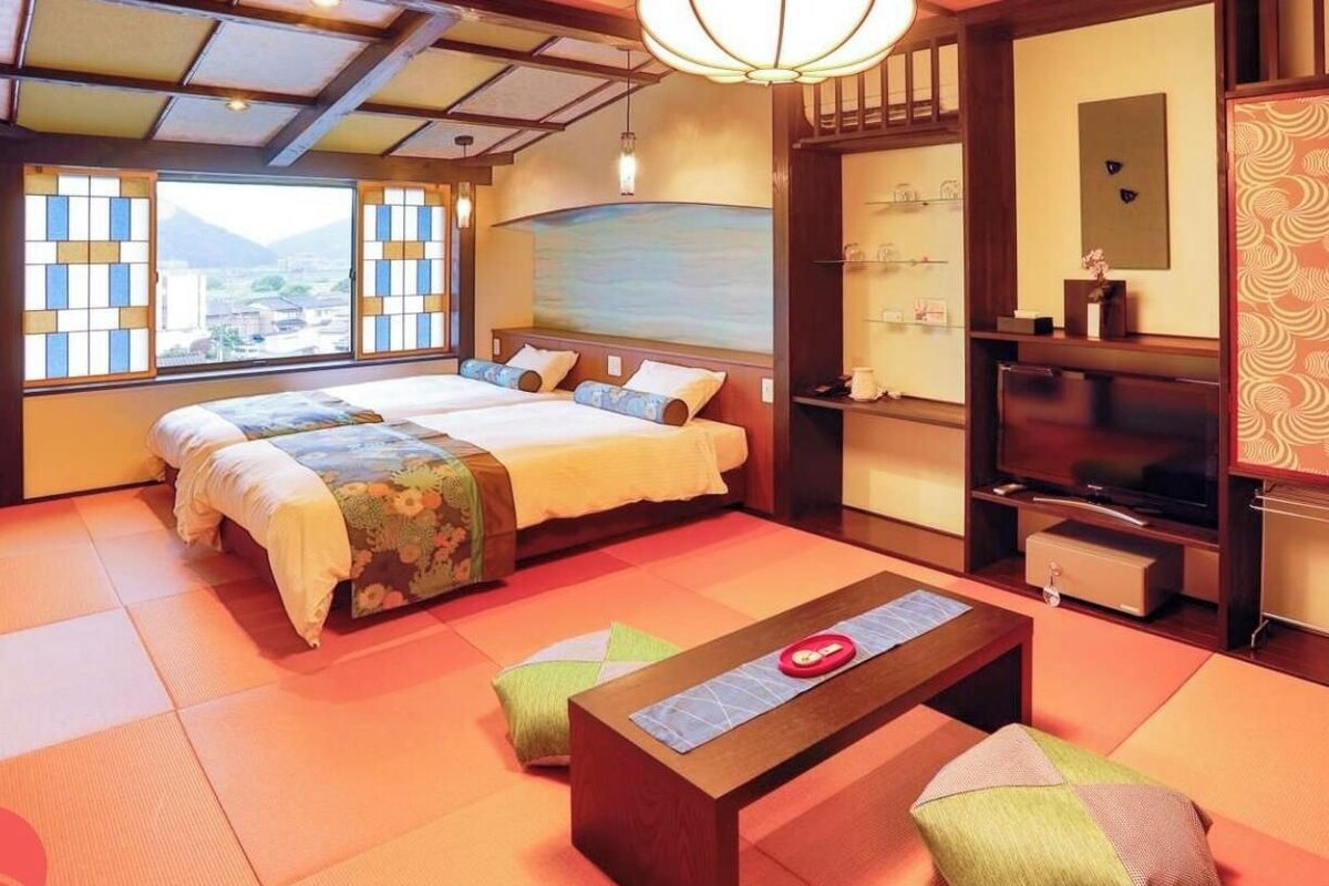 A traditional Japanese-style room with tatami flooring, a bed with a futon, a television, and a sliding door.