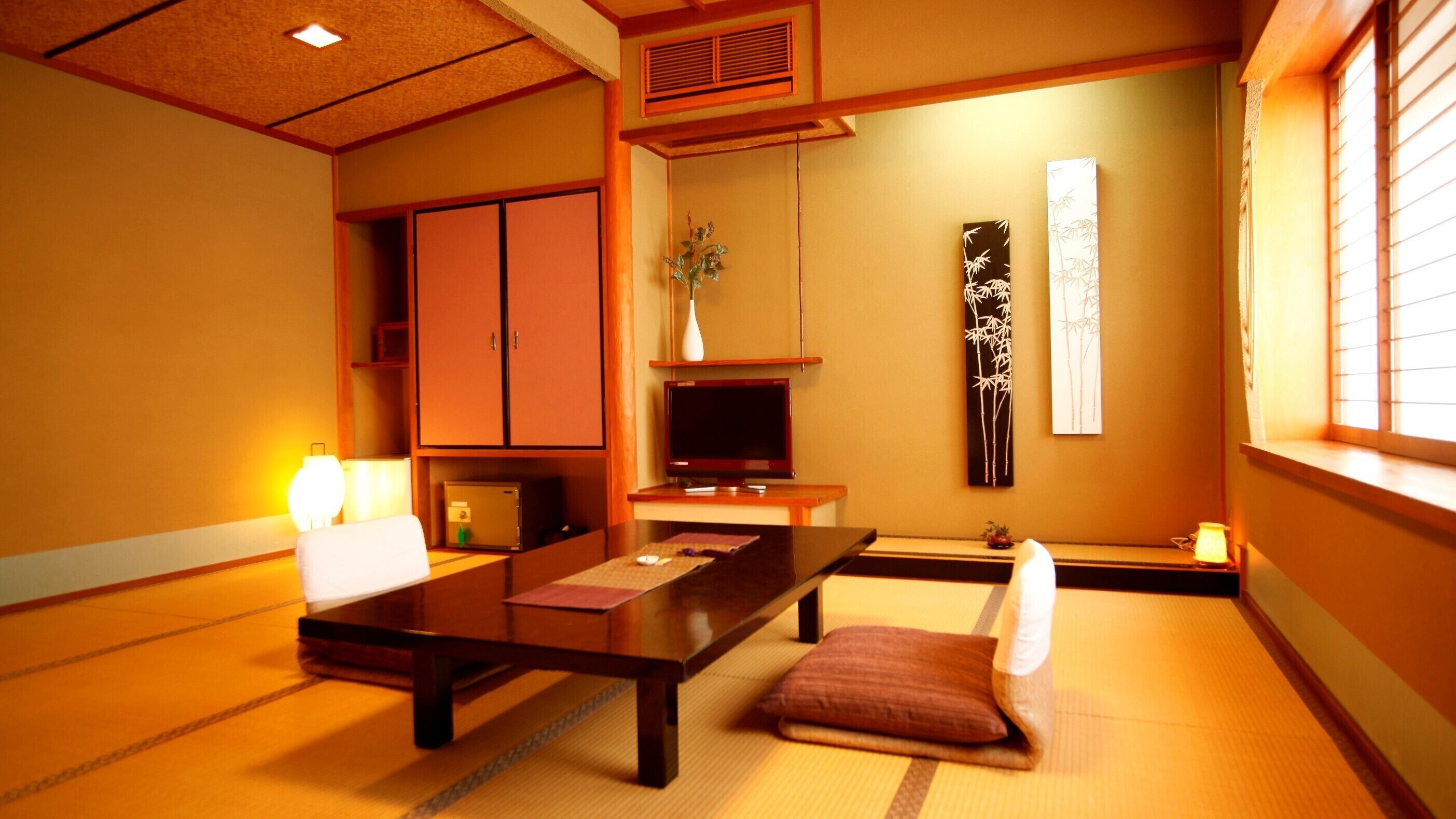 Una habitación tradicional japonesa con suelo de tatami, una mesa baja, un televisor y puertas correderas.