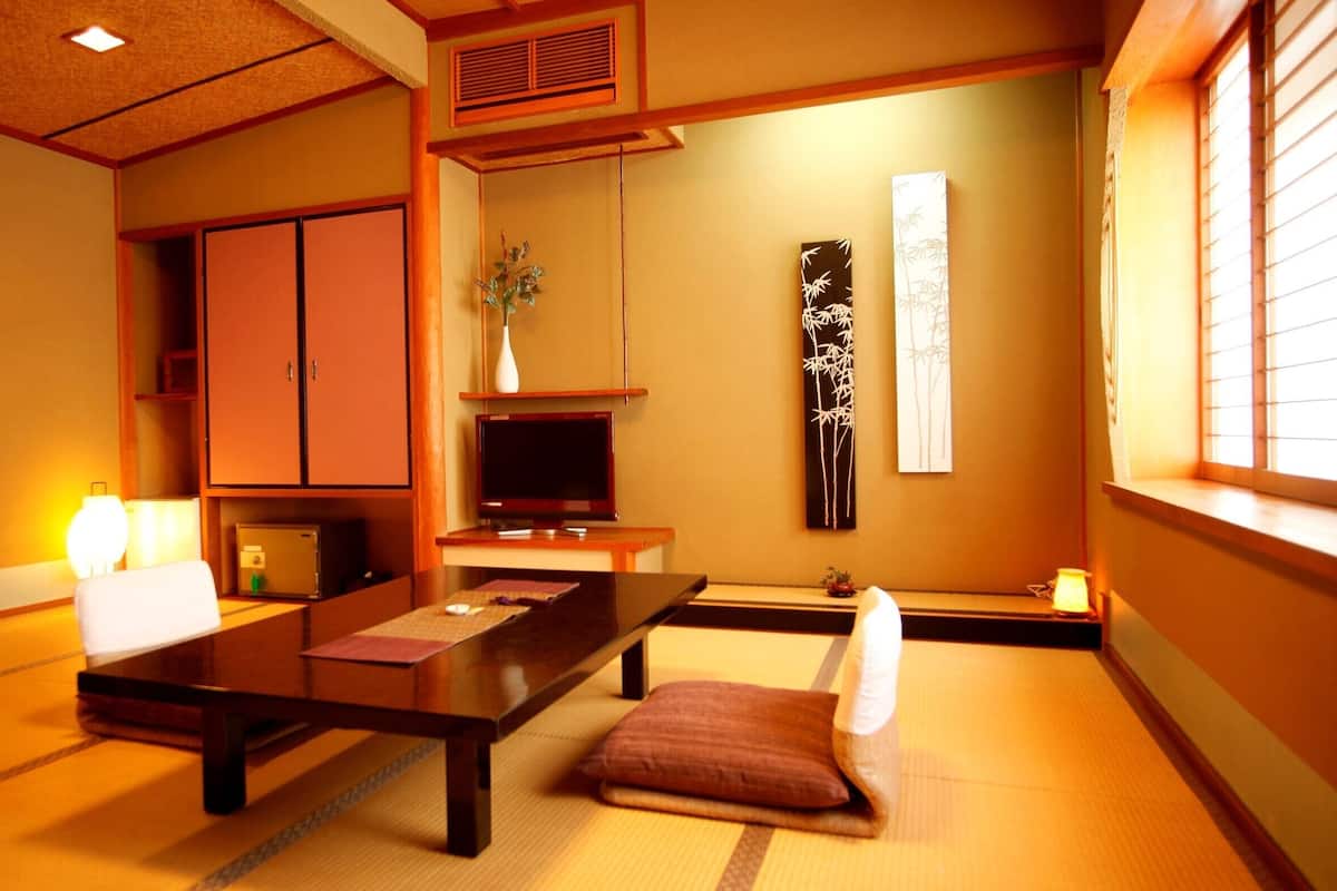Una habitación tradicional japonesa con suelo de tatami, una mesa baja, un televisor y puertas correderas.