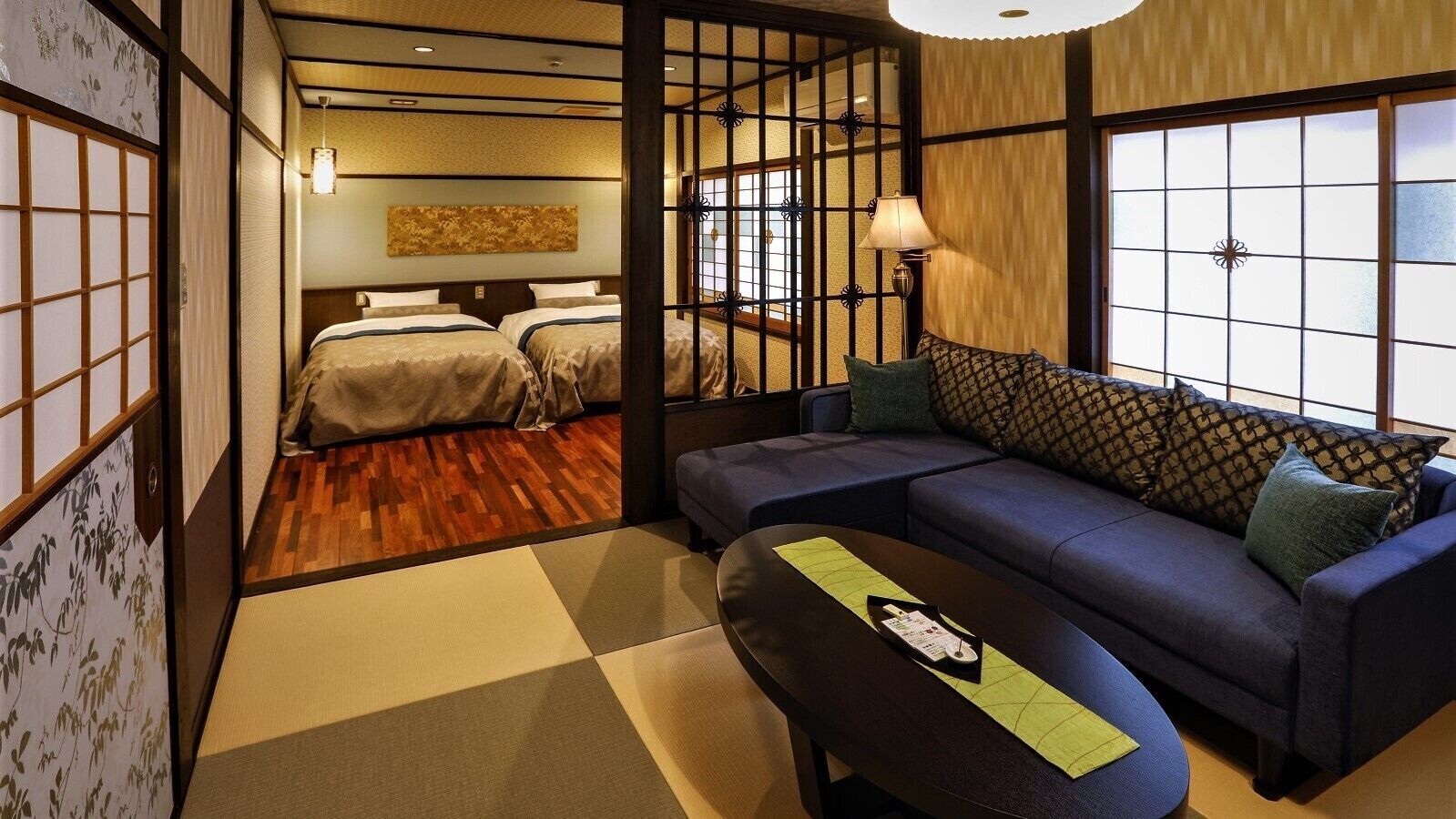 Una habitación tradicional japonesa con suelo de tatami, un futón, una mesita baja con posavasos y un sofá con cojines.