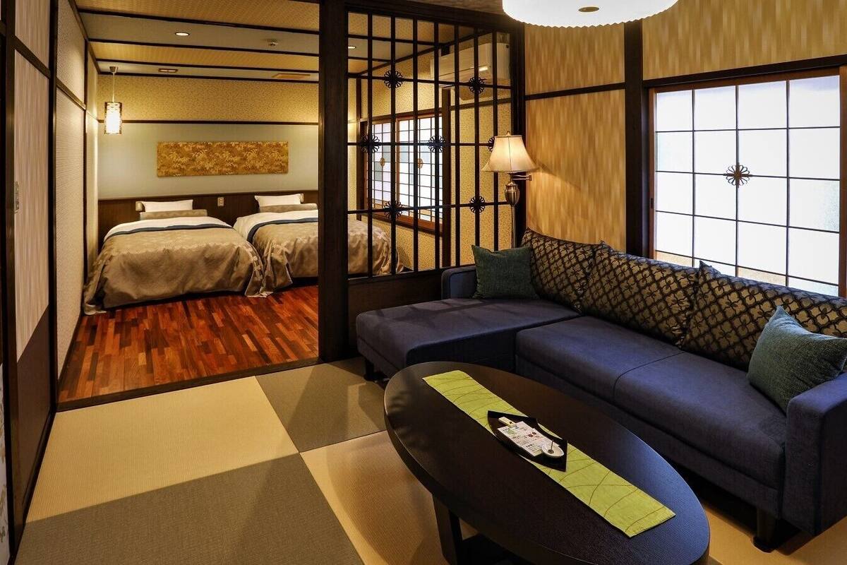 Ein traditioneller japanischer Raum mit Tatami-Boden, Futon-Bett, niedrigem Tisch mit Unterlage und einer Couch mit Kissen.
