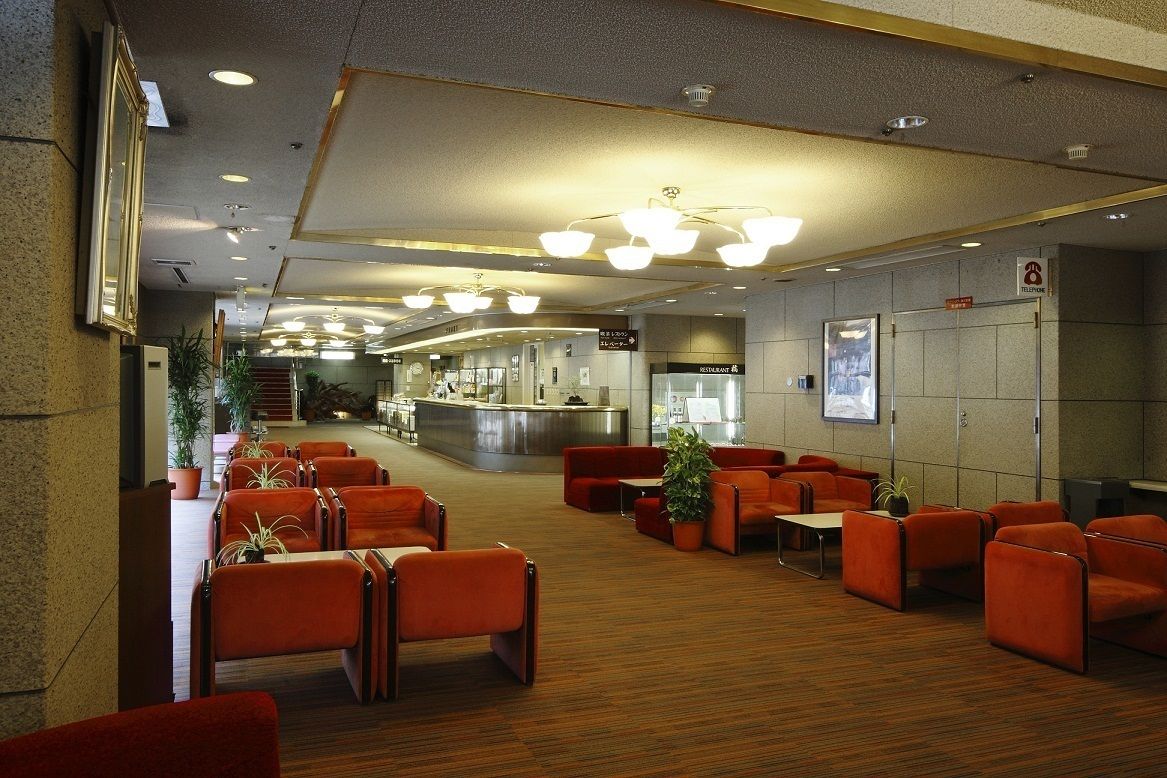 Un vestíbul d'hotel amb zones d'estar, una recepció i un restaurant al fons.
