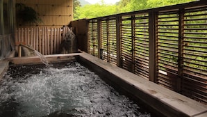 Un onsen japonais traditionnel, avec un bain en bois, des murs en bambou et une vue sur une végétation luxuriante.