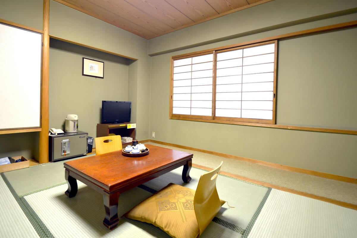 Een traditionele Japanse kamer met tatami vloerbedekking, een lage houten tafel, een televisie en een schuifdeur met shoji schermen.