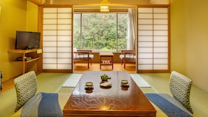 Une pièce de style japonais traditionnel, avec un sol recouvert de tatamis, une petite table basse avec un service à thé, des portes coulissantes en papier de riz (shoji) et un téléviseur posé sur une étagère.