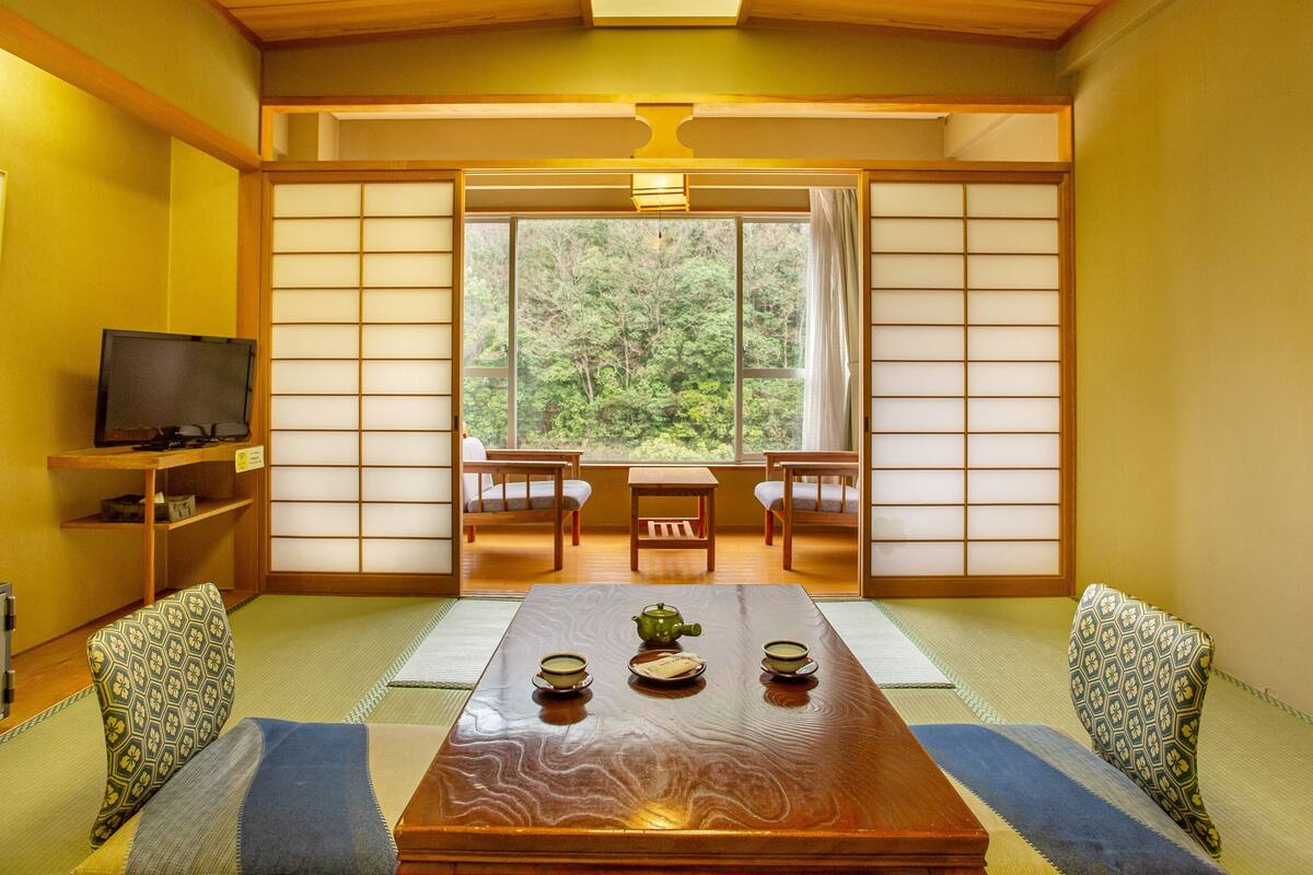 Een traditionele Japanse kamer met tatami vloerbedekking, een lage tafel met theeservies, schuifdeuren van shoji-papier en een televisie op een plank.