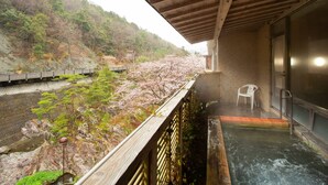 Un onsen japonais traditionnel doté d’une terrasse en bois offrant une vue sur une colline boisée.