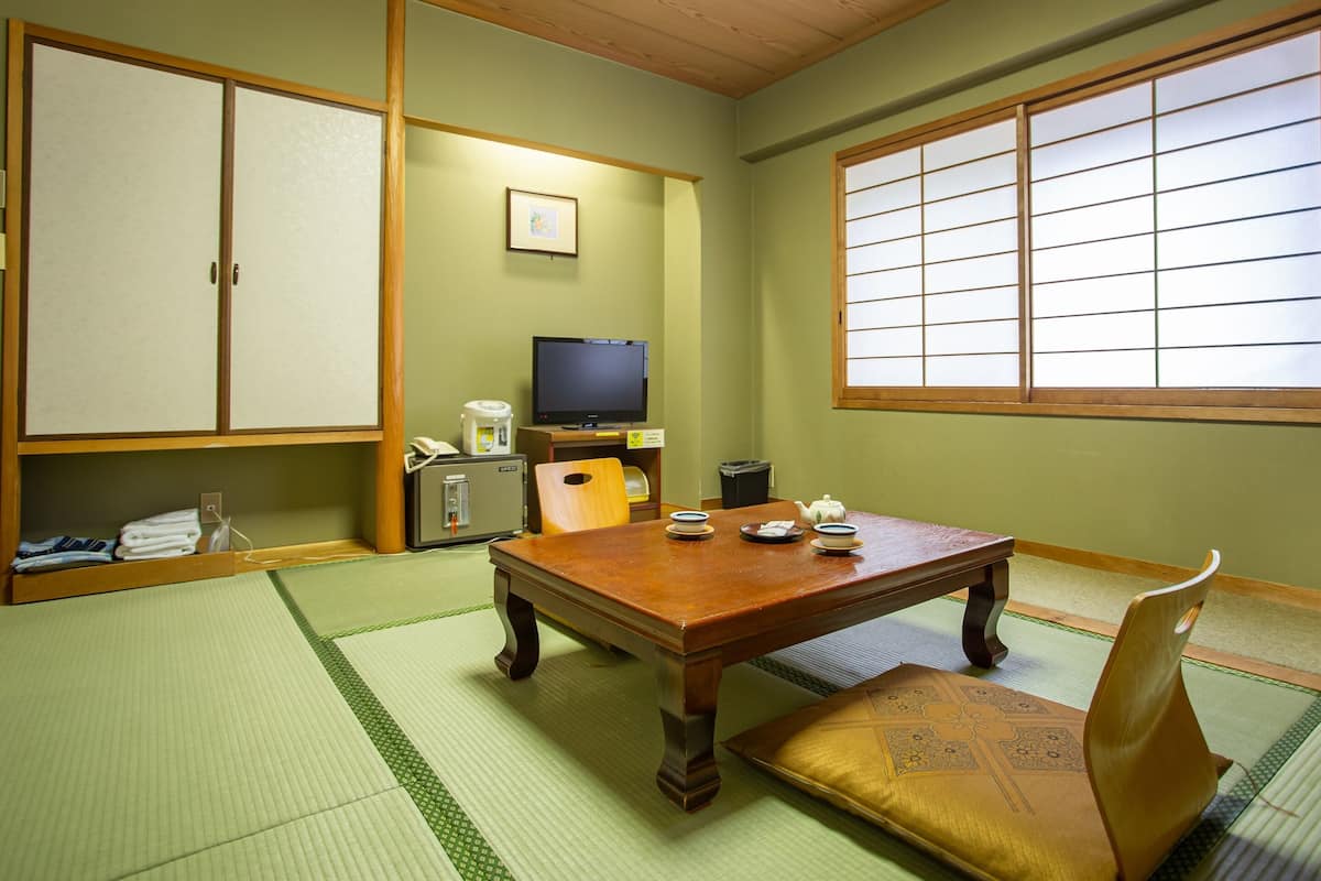 Een traditionele Japanse kamer met tatami vloerbedekking, een houten tafel, een televisie en schuifdeuren.