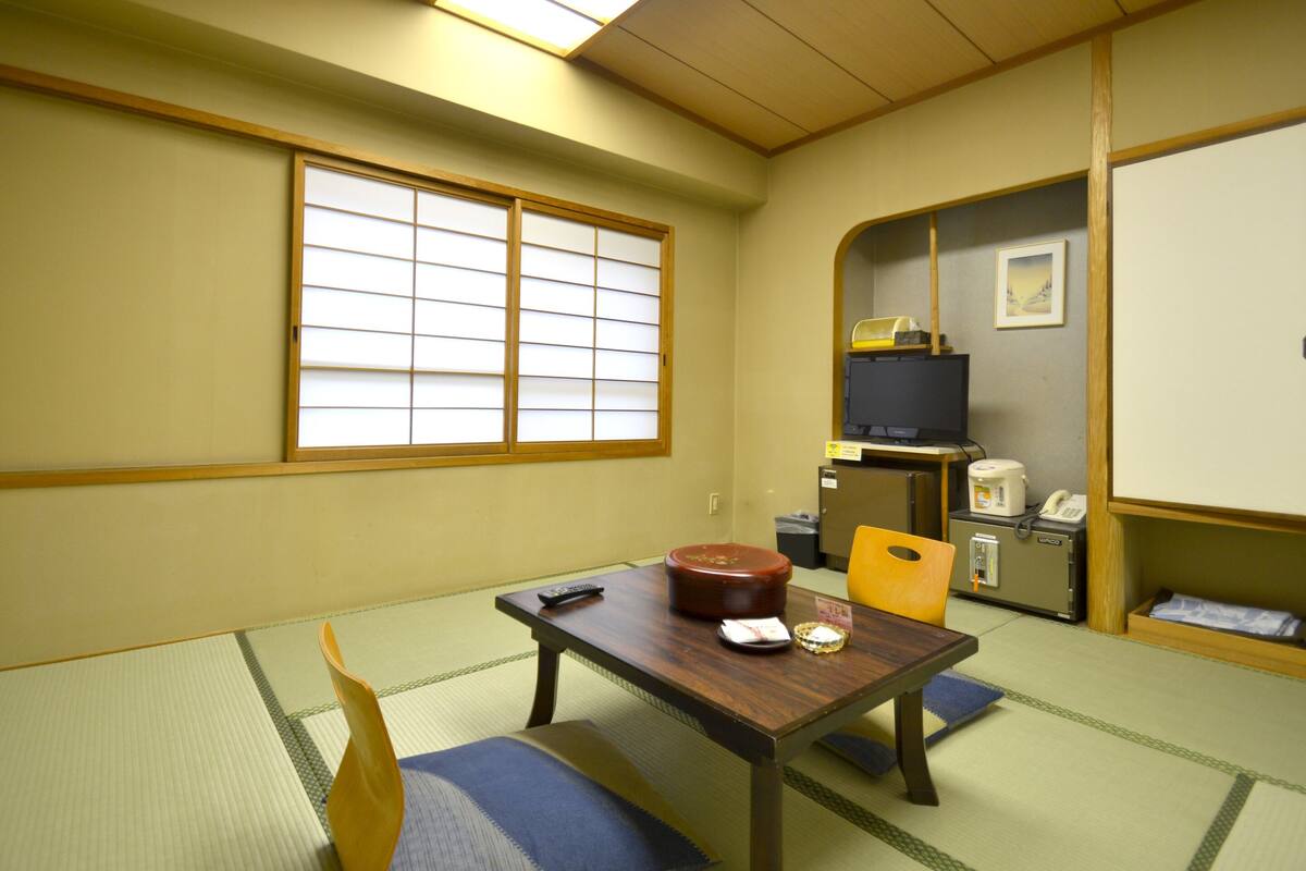 Een traditionele Japanse kamer met tatami vloeren, een lage tafel met een afstandsbediening, een televisie en een kleine koelkast.