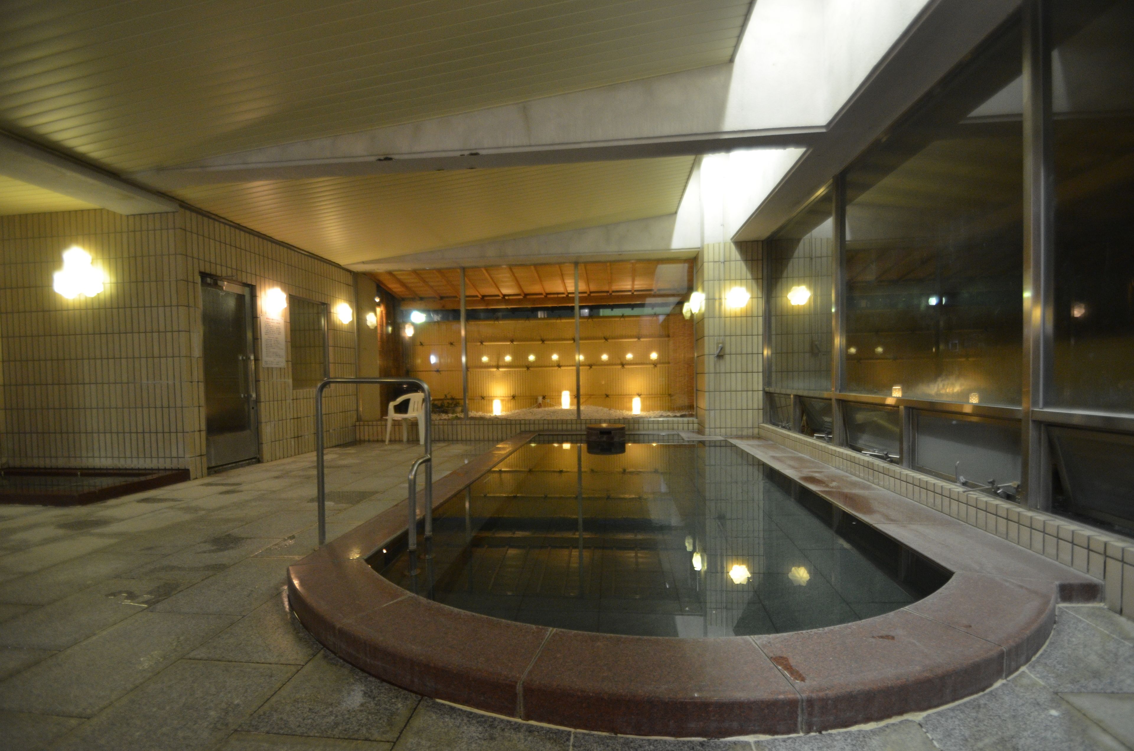 Piscina interna com paredes azulejadas, teto de madeira e estrutura de vidro.