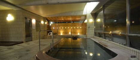 Piscina interna com paredes azulejadas, teto de madeira e estrutura de vidro.