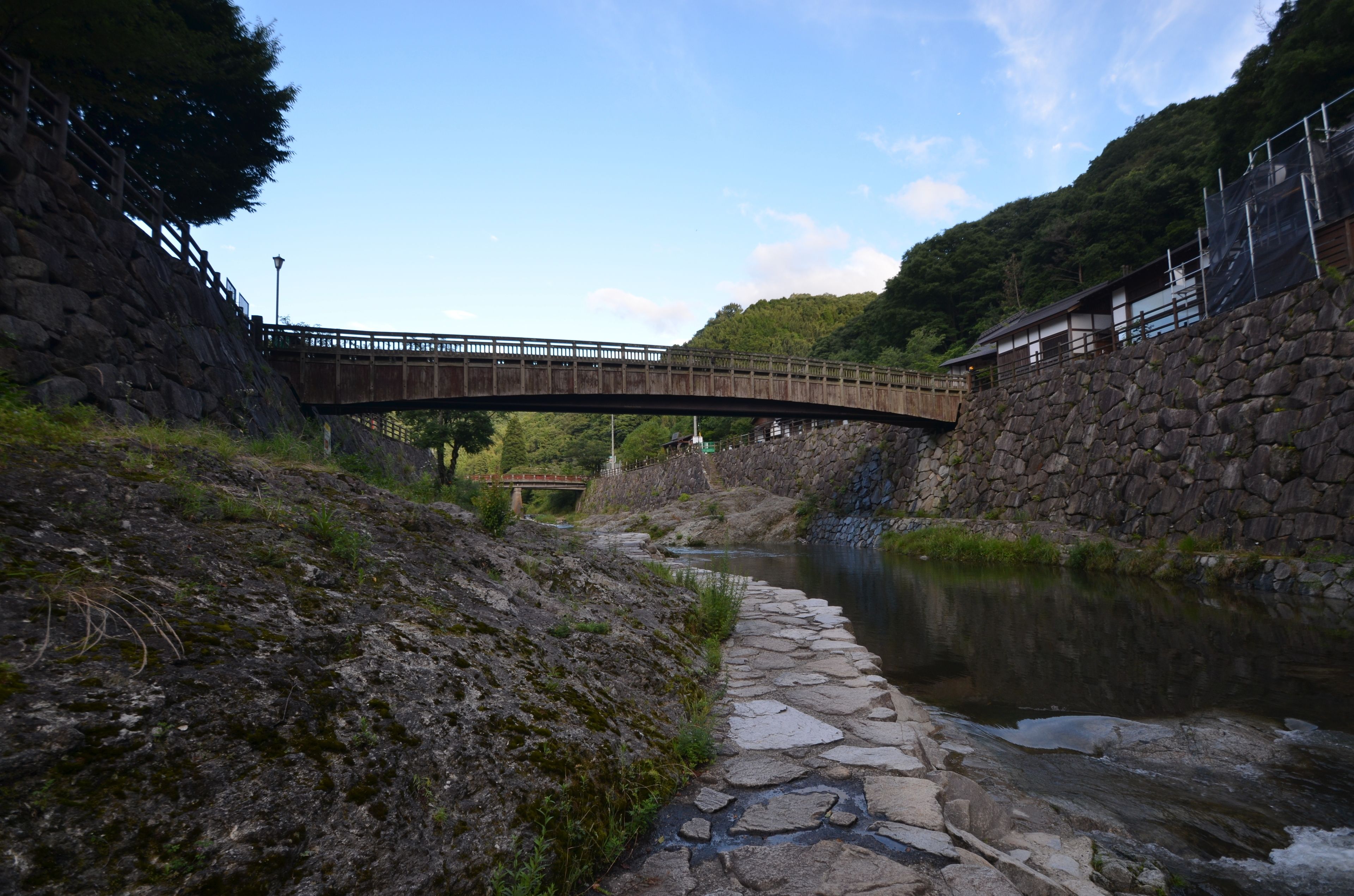 Un sendero de piedra junto a un río, un puente de madera y un muro de piedra.