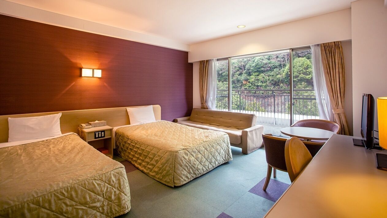 Une chambre d’hôtel avec deux lits, un canapé, un bureau et un balcon donnant sur un espace verdoyant.