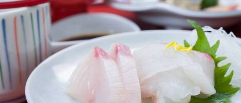 A plate of sashimi with a garnish of green leaves and yellow flowers, accompanied by a small bowl of soy sauce.