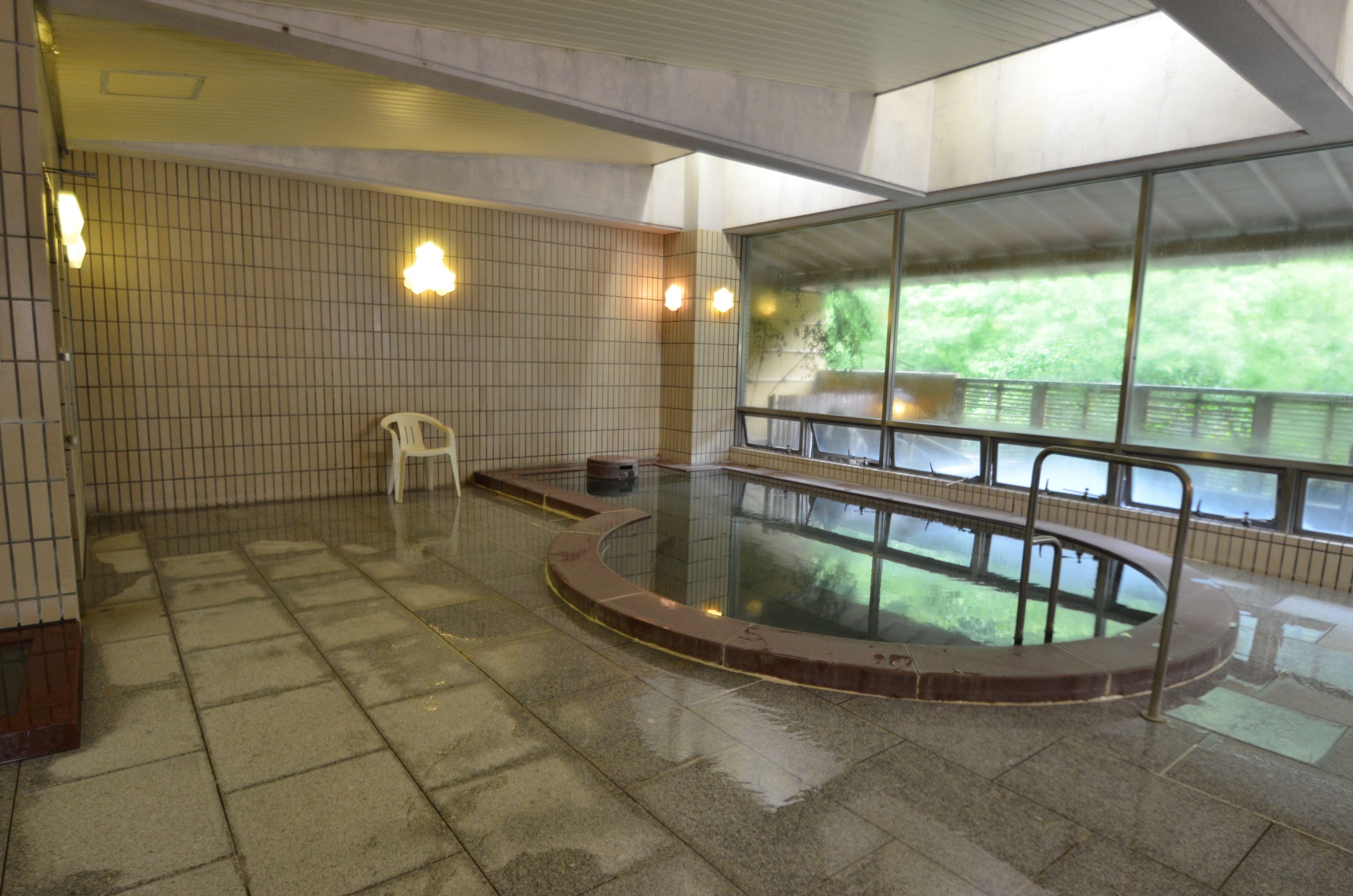 A swimming pool with a tiled floor and a view of greenery outside.