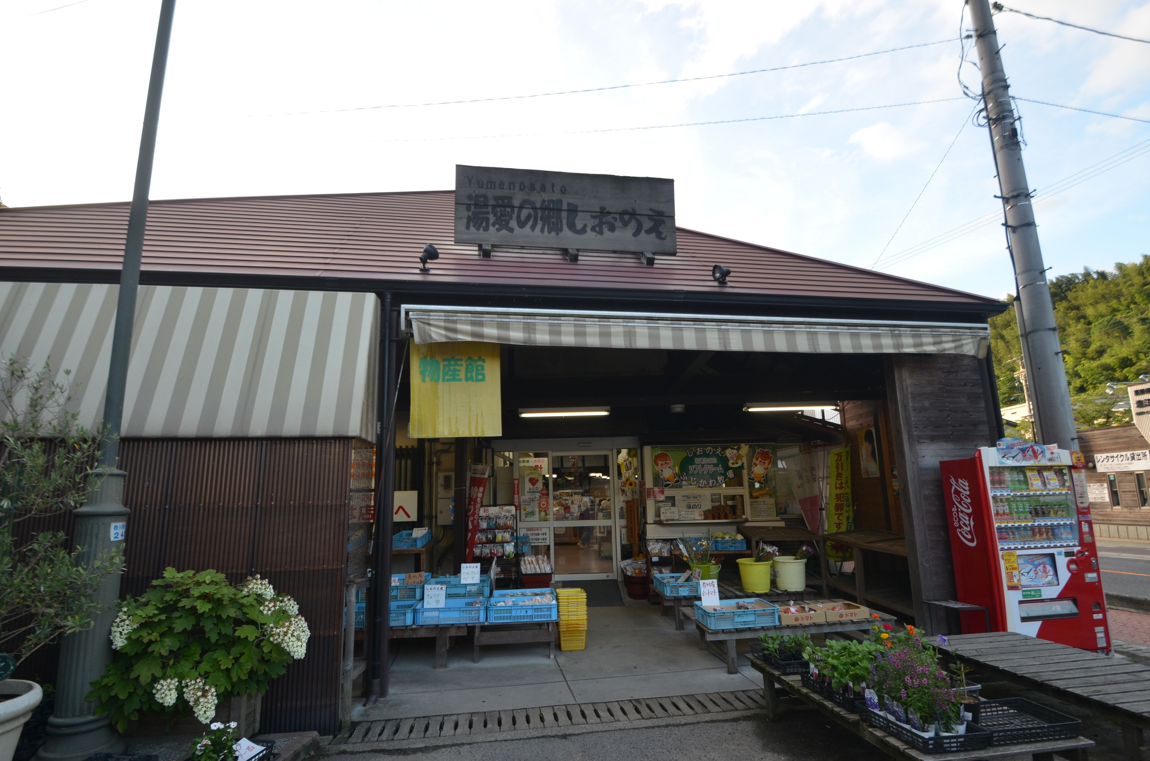 A storefront with a sign in a foreign language, a Coca-Cola vending machine, and various items displayed outside.