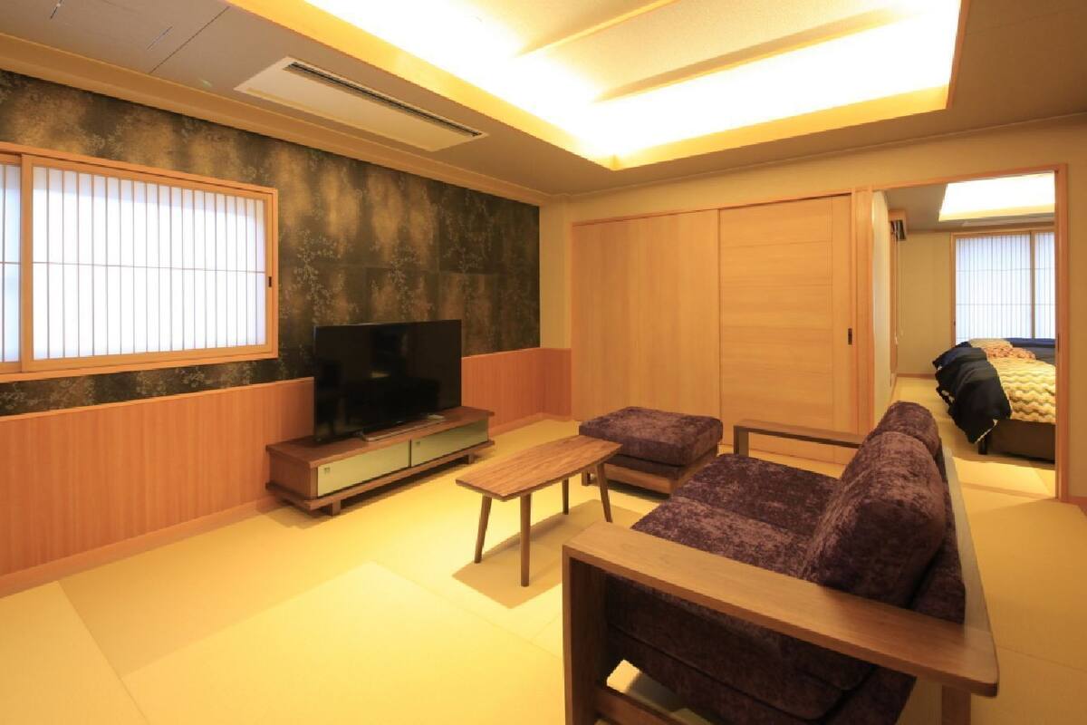 A traditional Japanese-style living room with tatami flooring, a low wooden table, a sofa, and a television.