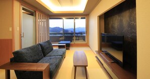 Un salon moderne avec un canapé, une table basse et un téléviseur. Une porte coulissante donne accès à un balcon offrant une vue sur les montagnes.