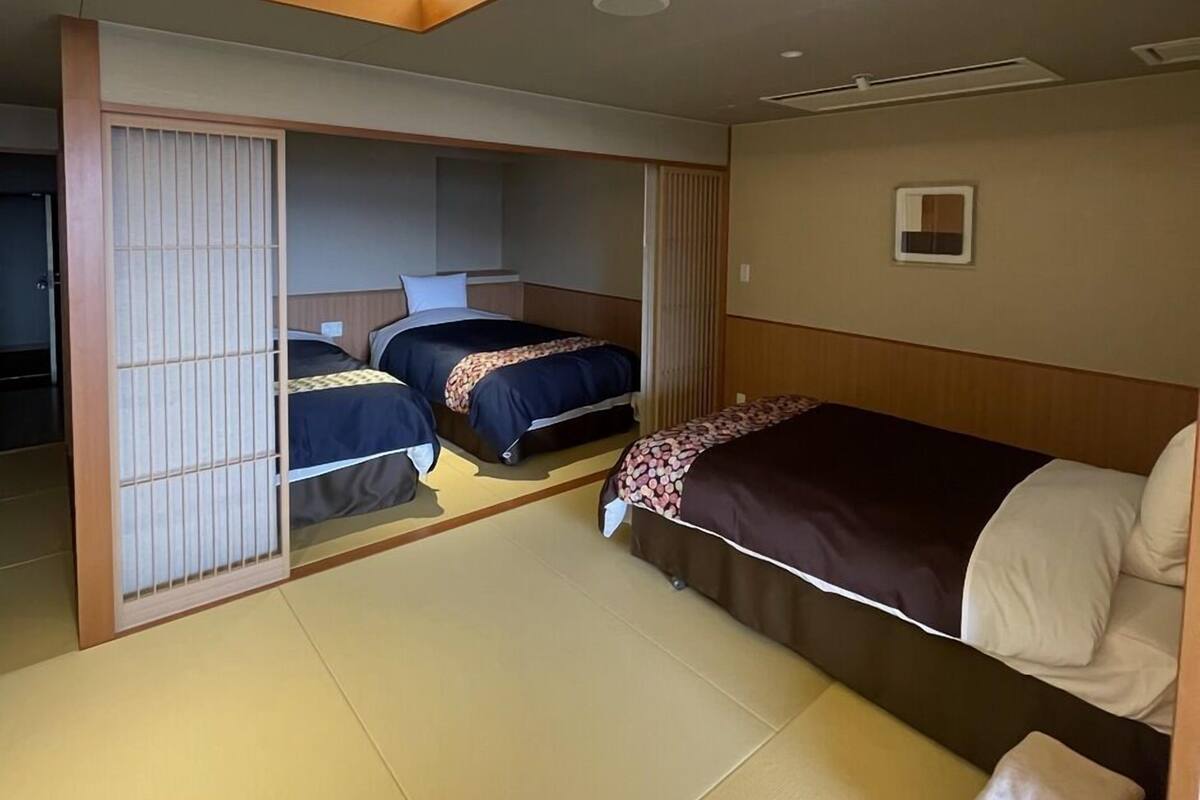 A hotel room with two beds, a sliding door, and a small window.