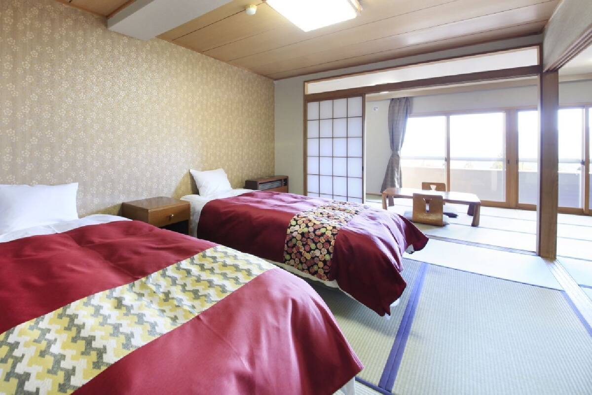 A hotel room with two beds, a wooden ceiling, a traditional Japanese sliding door, and tatami mat flooring.