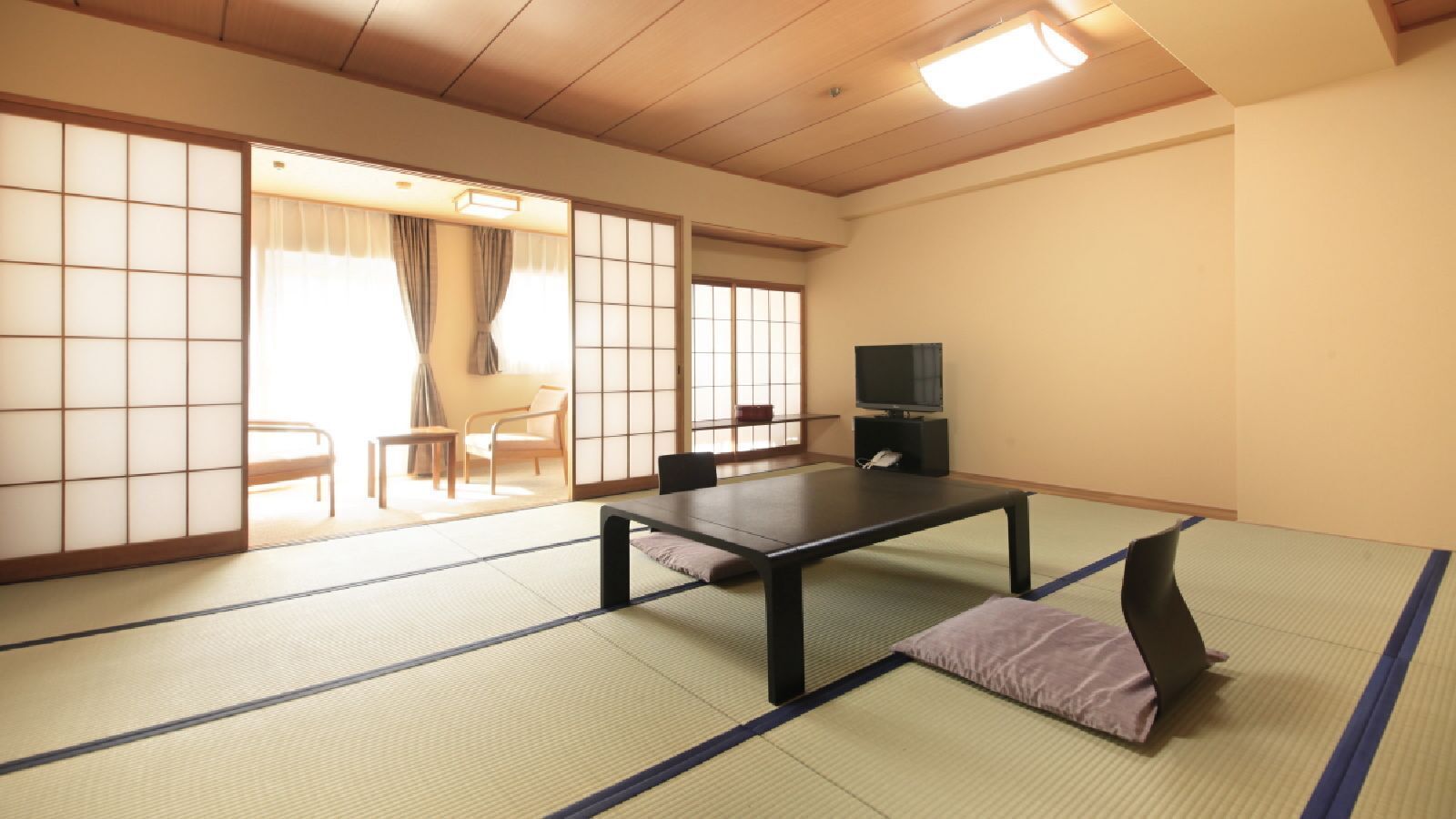 A tatami mat room with a low table, chairs, a television, and sliding doors.