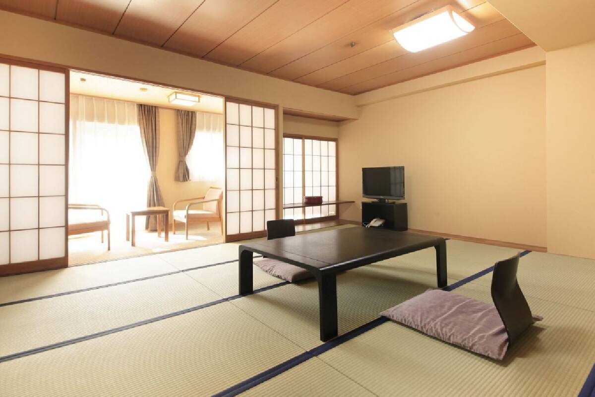 A tatami mat room with a low table, chairs, a television, and sliding doors.