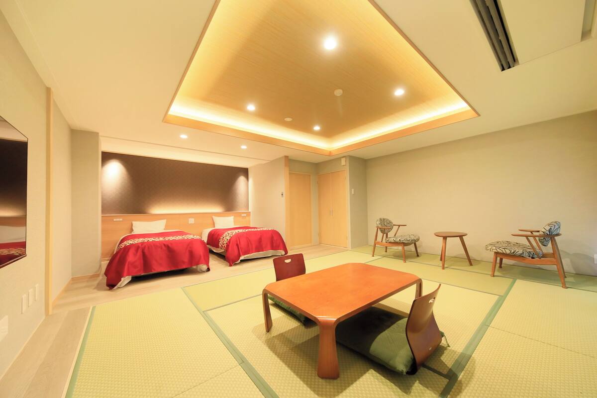 A hotel room with two beds, a dining table, chairs, and a small seating area.