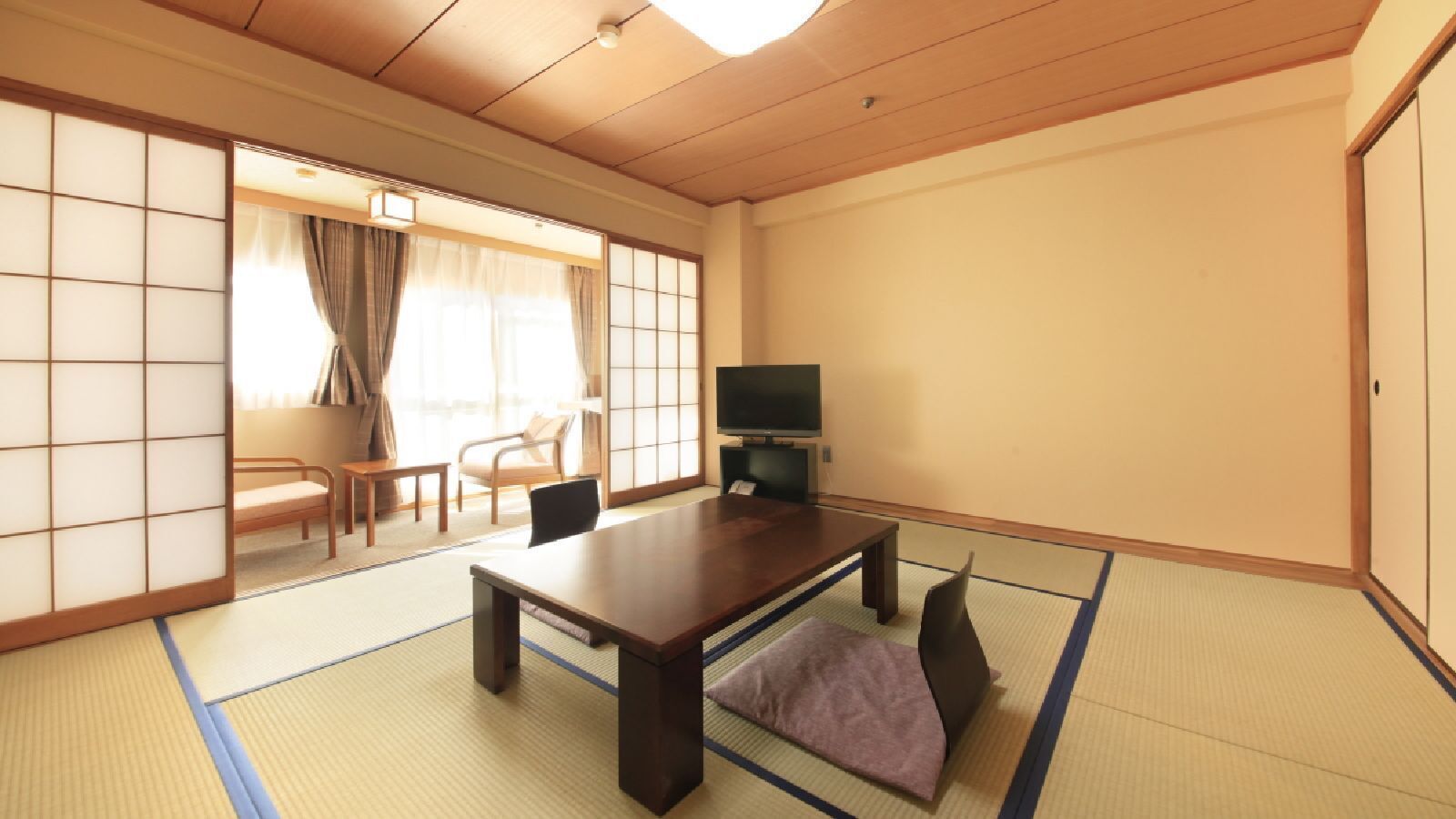 A traditional Japanese room with tatami flooring, a low table, a television, and sliding doors.