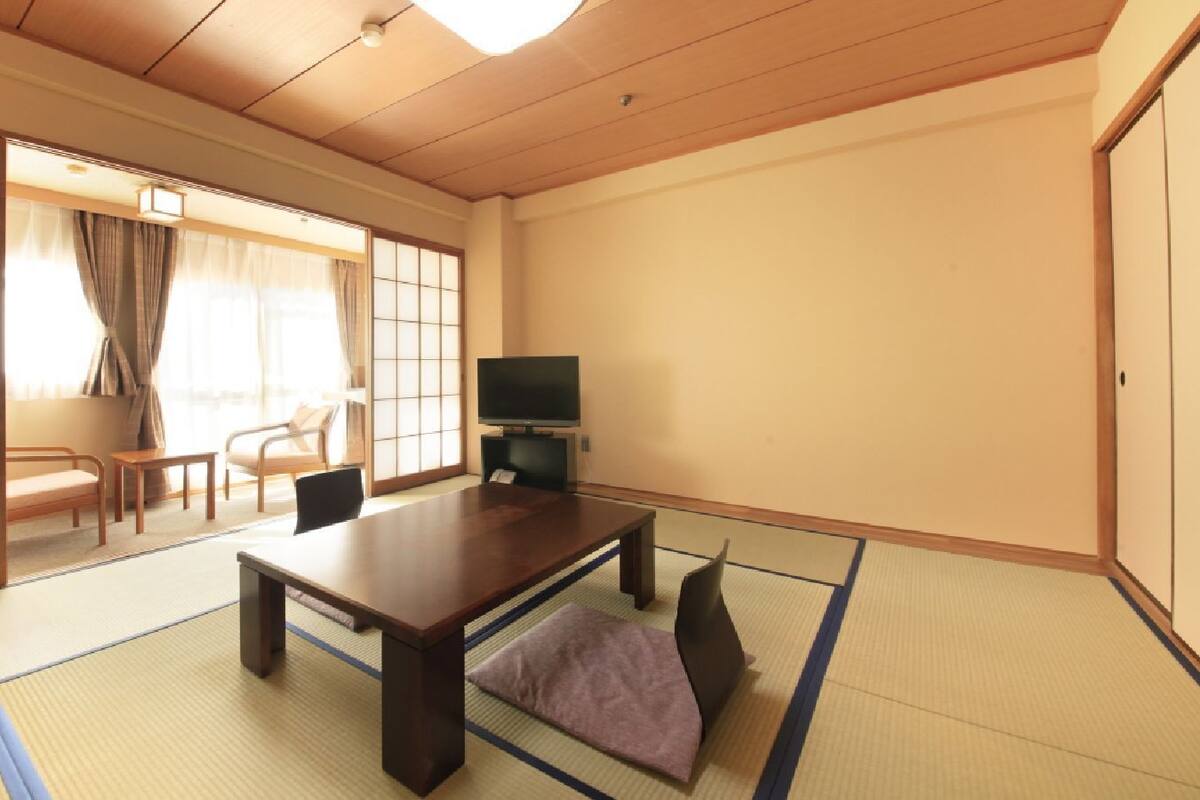 A traditional Japanese room with tatami flooring, a low table, a television, and sliding doors.