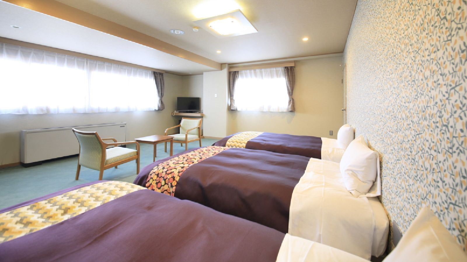 A hotel room with three beds, a desk, a chair, and a television.