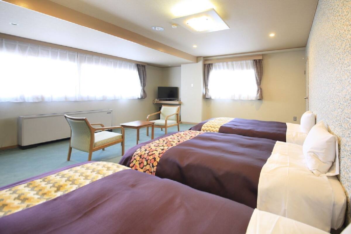 A hotel room with three beds, a desk, a chair, and a television.