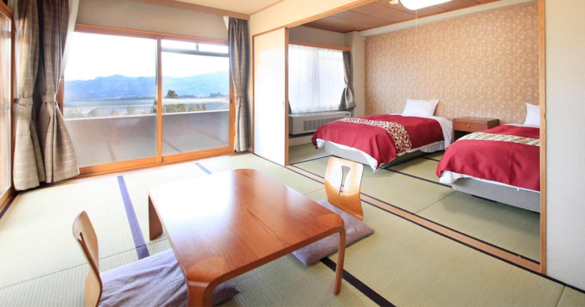 Een hotelkamer met een schuifdeur naar een balkon, een bed met rode beddengoed, een houten tafel en een stoel.