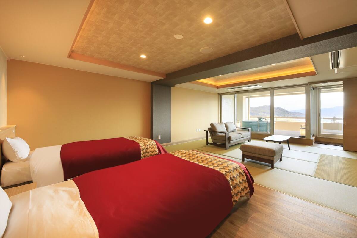 A hotel room with two beds, a sofa, a small table, and a view of the outdoors.